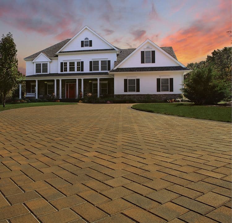 A closeup of a light brown paver driveway in front of a white home