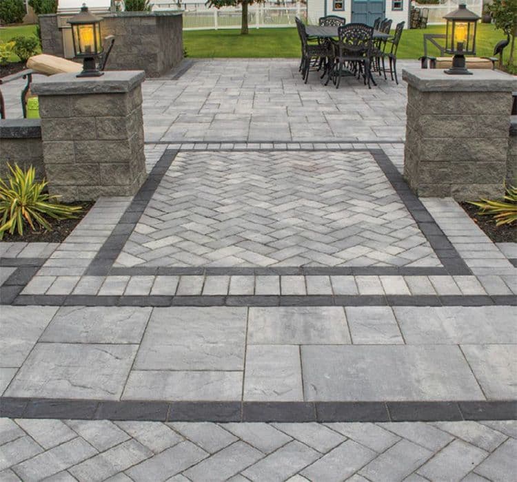 A grill and outdoor eating area with gray pavers in an inlay pattern.