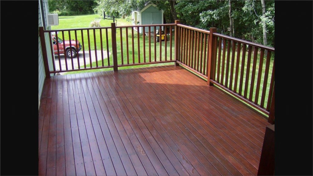 A closeup of a mahogany deck with mahogany handrails. You can see little bits of a front yard and driveway in the background.